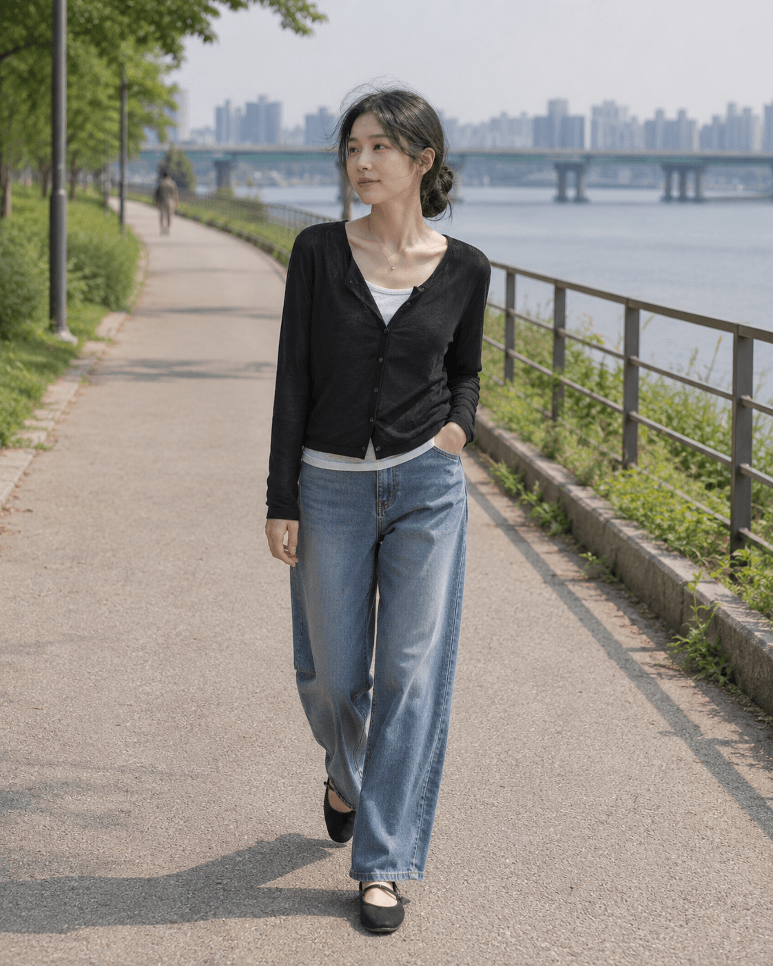 Editorial wearing shot of a black sheer cardigan, light gray tee, wide-leg jeans, and black Mary Jane flats near a riverside walkway